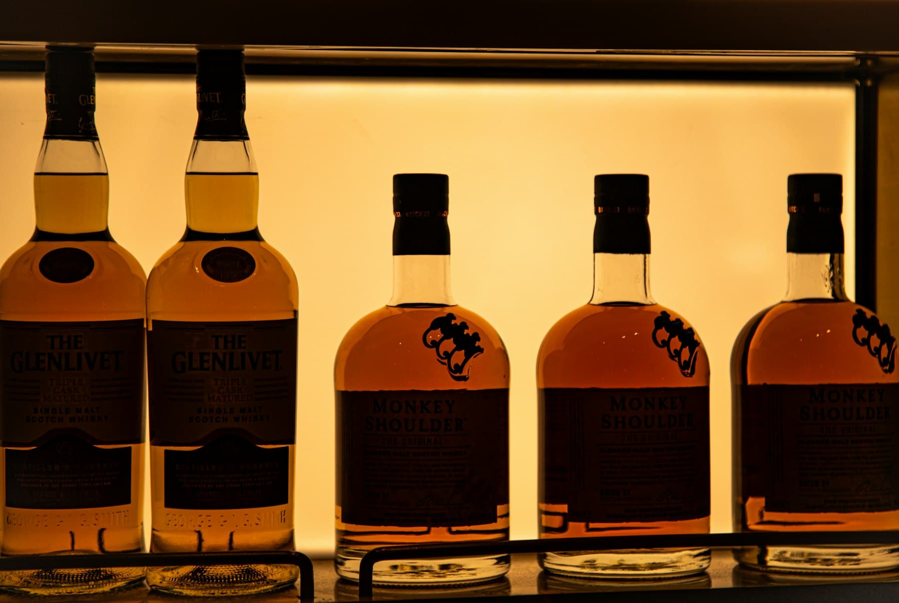 A row of whisky bottles on a backlit bar shelf
