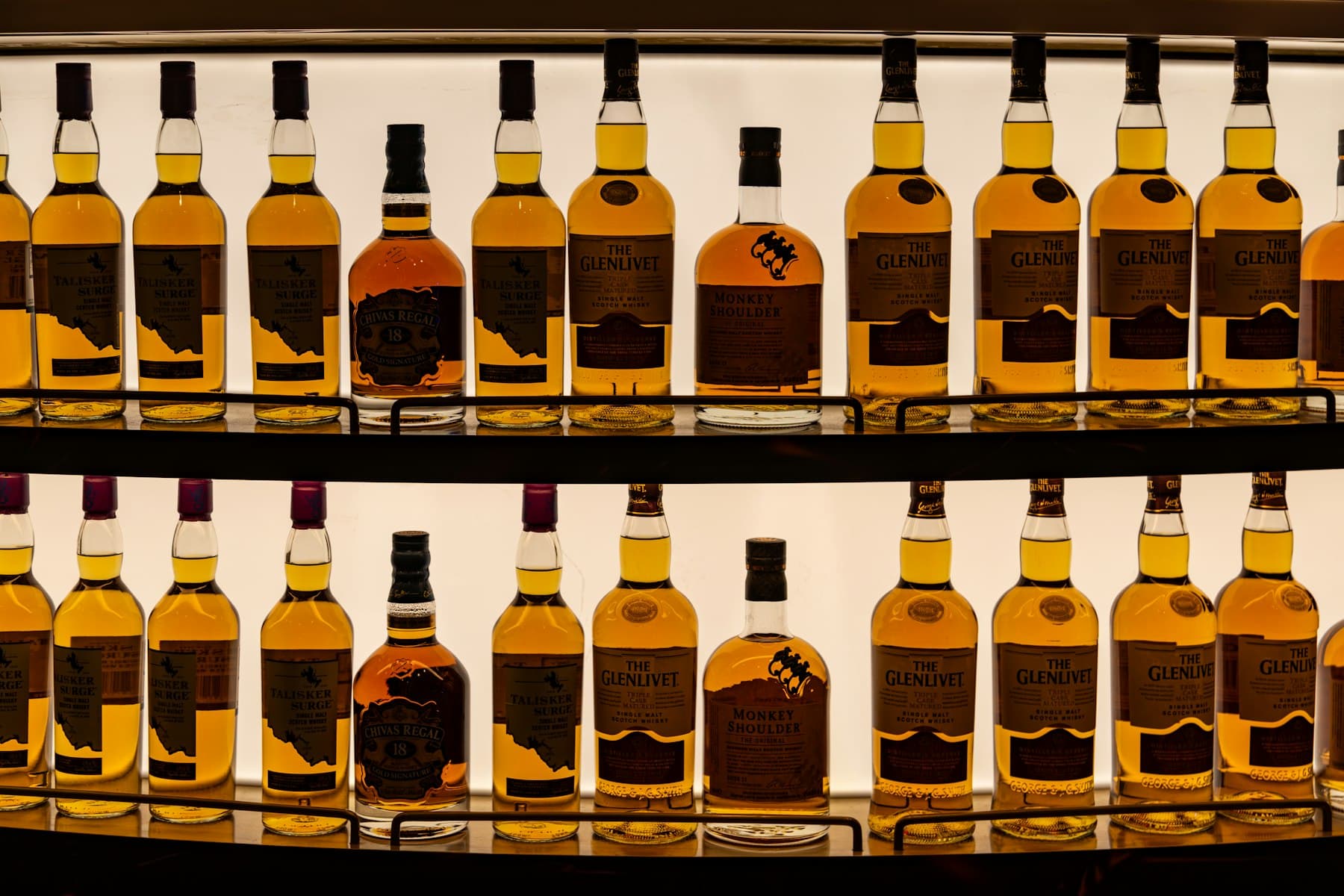 Two backlit shelves of scotch bottles on a back bar
