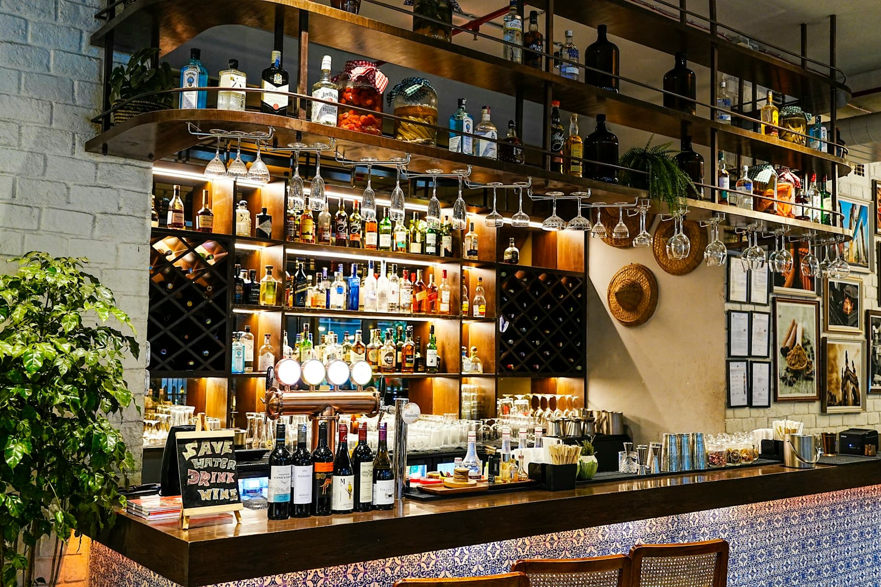 An empty, well-stocked bar counter with taps and hanging glasses in daylight