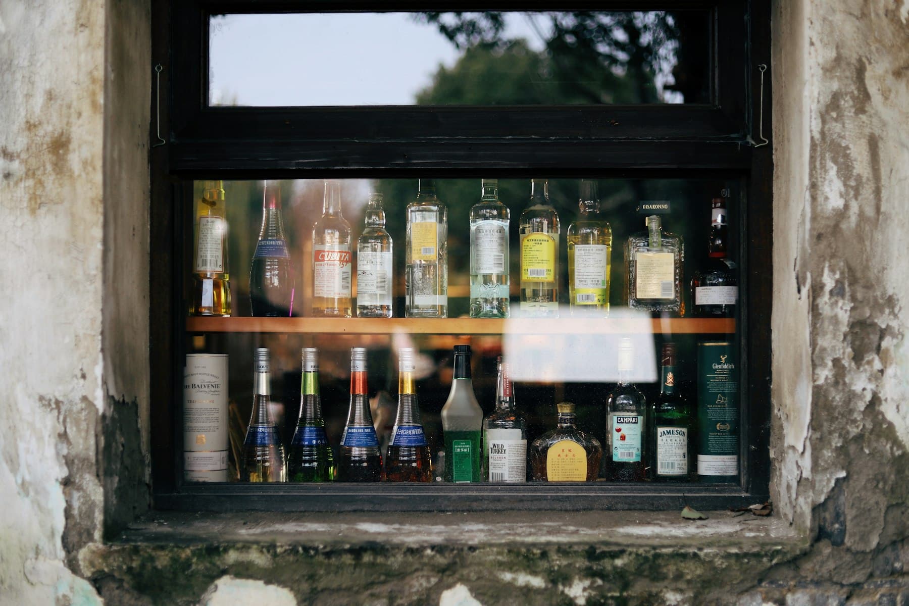 Assorted liquor bottles on two shelves behind a bar window